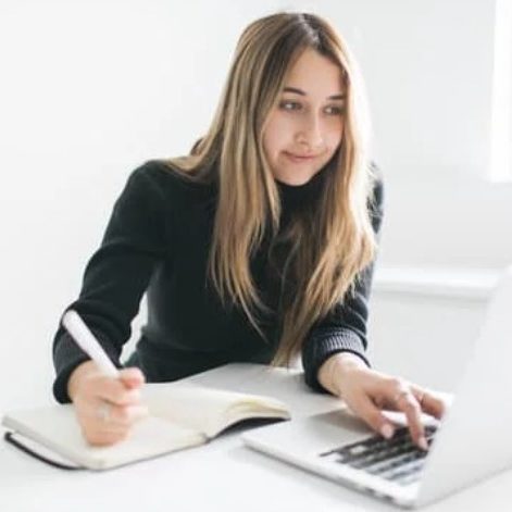 Young woman on a laptop with one hand and writing in a notebook with the other